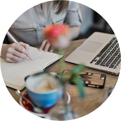 Close-up of a woman writing in a notebook near a laptop, symbolizing content planning.